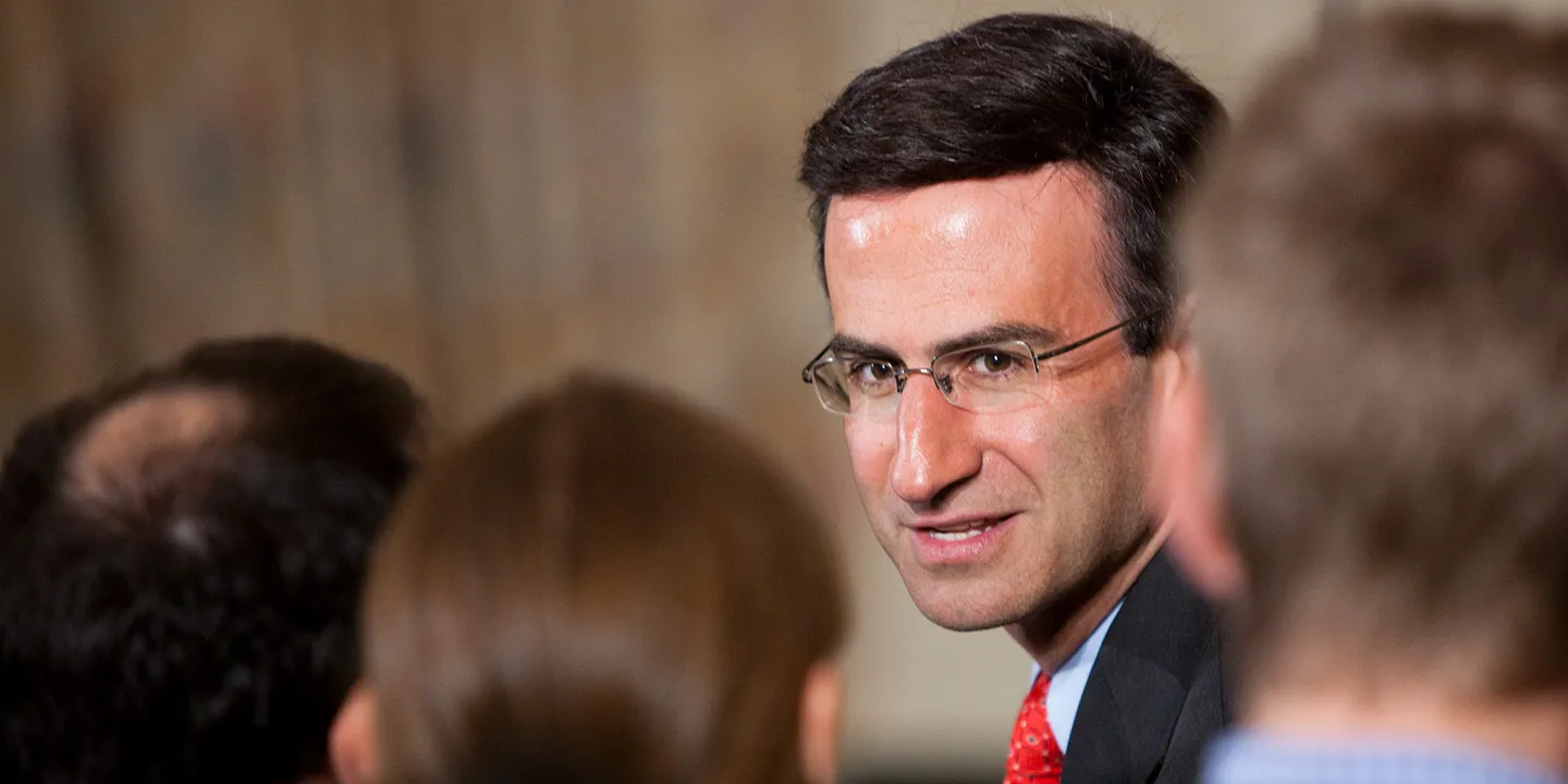 Peter Orszag with neatly styled dark hair and glasses, wearing a suit and red tie while speaking in a professional setting.